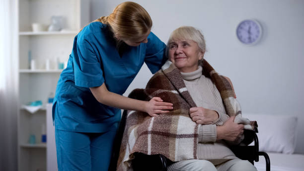 Kind nurse covering with blanket handicapped old woman, hospital care, service
